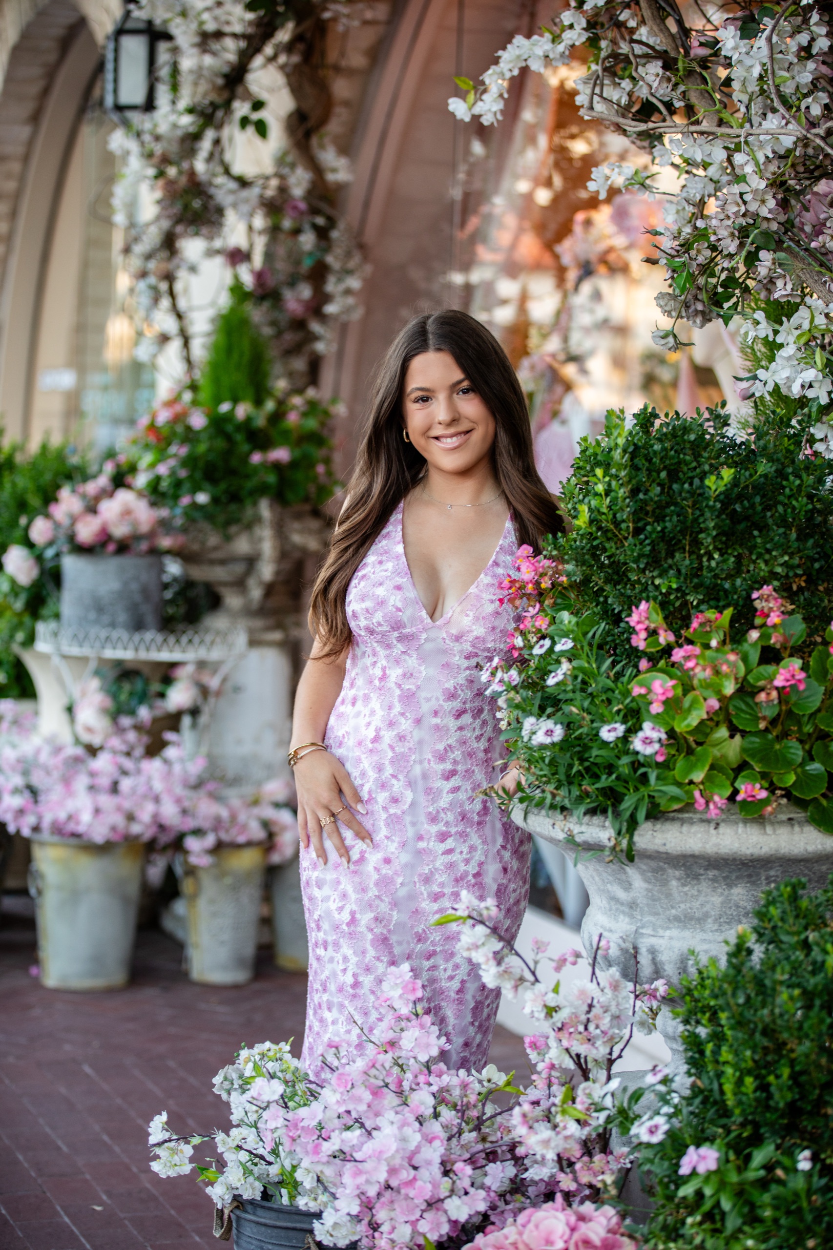Senior in a pink floral dress among blossoms outside a flower shop