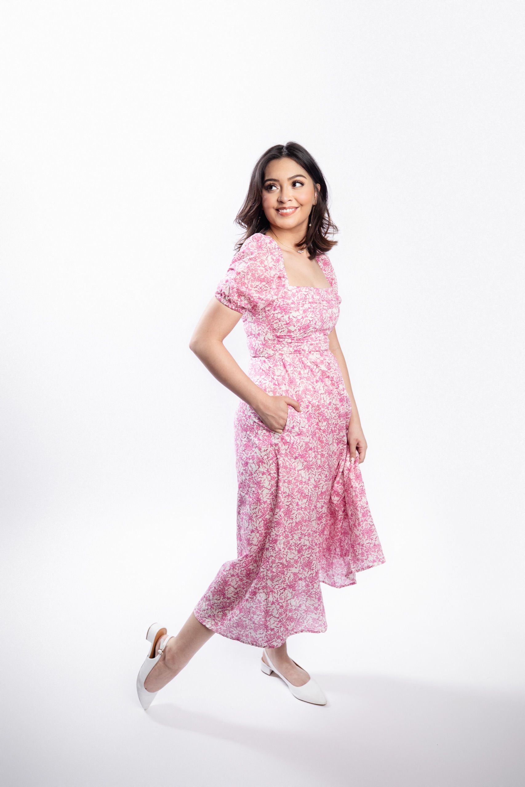 Senior twirling a pink floral midi dress in a bright white studio